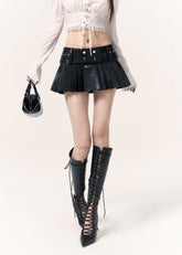 Black low-rise PU mini skort with pleats, a faux belt, and rivet buckle details