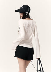 White long-sleeve top with an angel wing back print styled with a black mini skirt and cap
