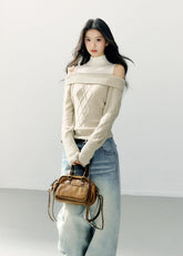 Model wearing an ivory asymmetric one-shoulder cable-knit sweater