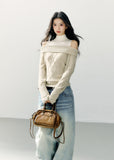 Model wearing an ivory asymmetric one-shoulder cable-knit sweater