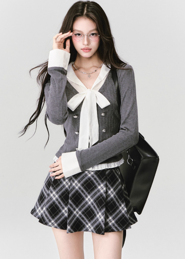 A soft rebellion in knit form — this double-breasted faux two-piece top blends vintage academia with K-fashion sensuality. The ivory bow and pleated trim contrast against charcoal grey, creating a refined silhouette that flatters with quiet confidence. Perfect for 2025 fall looks that balance grace and edge.