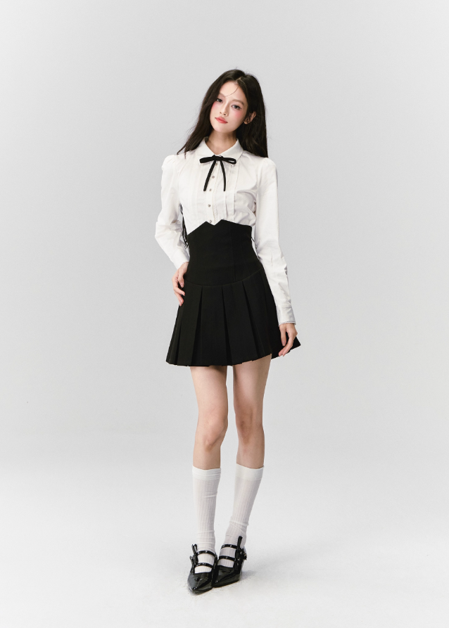 The Cherry Blossom Sonata Set captures the duality of innocence and control — a signature Fragileheart silhouette. The crisp ivory blouse, adorned with a black ribbon tie, flows into a high-waisted pleated skirt that sculpts the waist with subtle strength. Inspired by moonlit refinement and poetic order, it’s a quiet statement of authority wrapped in grace.