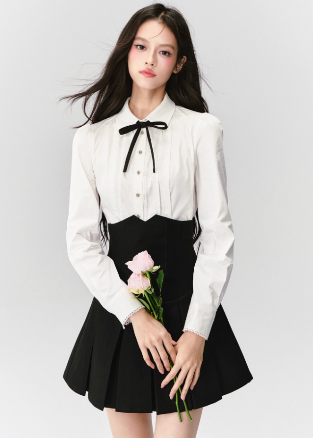 The Cherry Blossom Sonata Set captures the duality of innocence and control — a signature Fragileheart silhouette. The crisp ivory blouse, adorned with a black ribbon tie, flows into a high-waisted pleated skirt that sculpts the waist with subtle strength. Inspired by moonlit refinement and poetic order, it’s a quiet statement of authority wrapped in grace.
