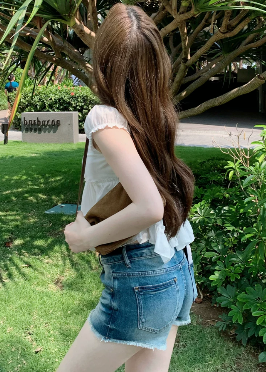 low rise denim shorts, vintage denim shorts, fringe denim shorts, distressed denim shorts, cat whisker shorts, American vintage shorts, women’s hot shorts, casual denim shorts, summer denim shorts, frayed hem shorts, Korean feminine styling, resort denim shorts, cotton blend denim shorts, washed denim shorts, vacation shorts outfit