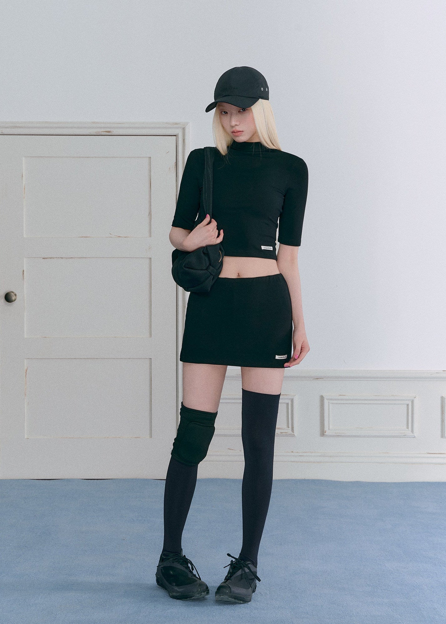 Model wearing a black half-turtleneck knit top and A-line mini skirt set