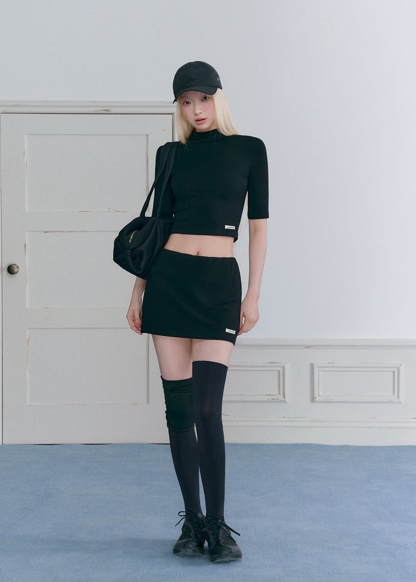 Model wearing a black half-turtleneck knit top and A-line mini skirt set