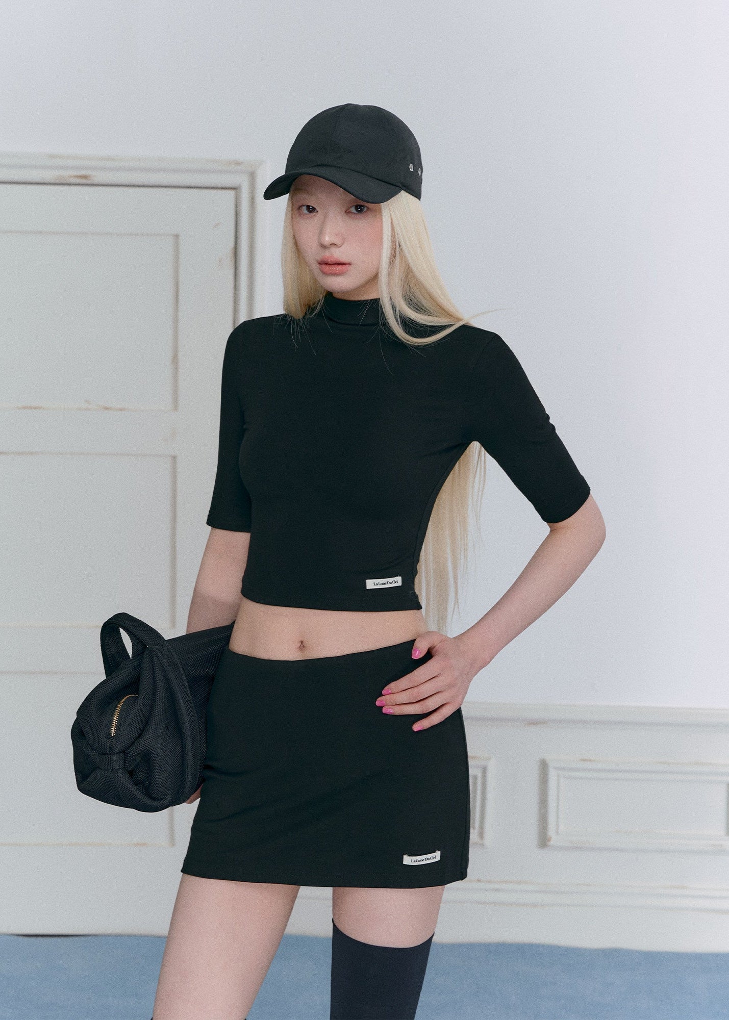 Model wearing a black half-turtleneck knit top and A-line mini skirt set