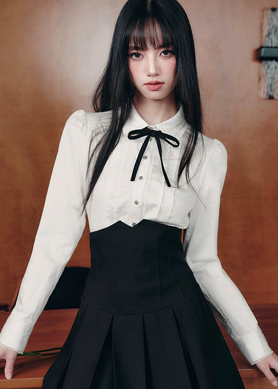 The Cherry Blossom Sonata Set captures the duality of innocence and control — a signature Fragileheart silhouette. The crisp ivory blouse, adorned with a black ribbon tie, flows into a high-waisted pleated skirt that sculpts the waist with subtle strength. Inspired by moonlit refinement and poetic order, it’s a quiet statement of authority wrapped in grace.