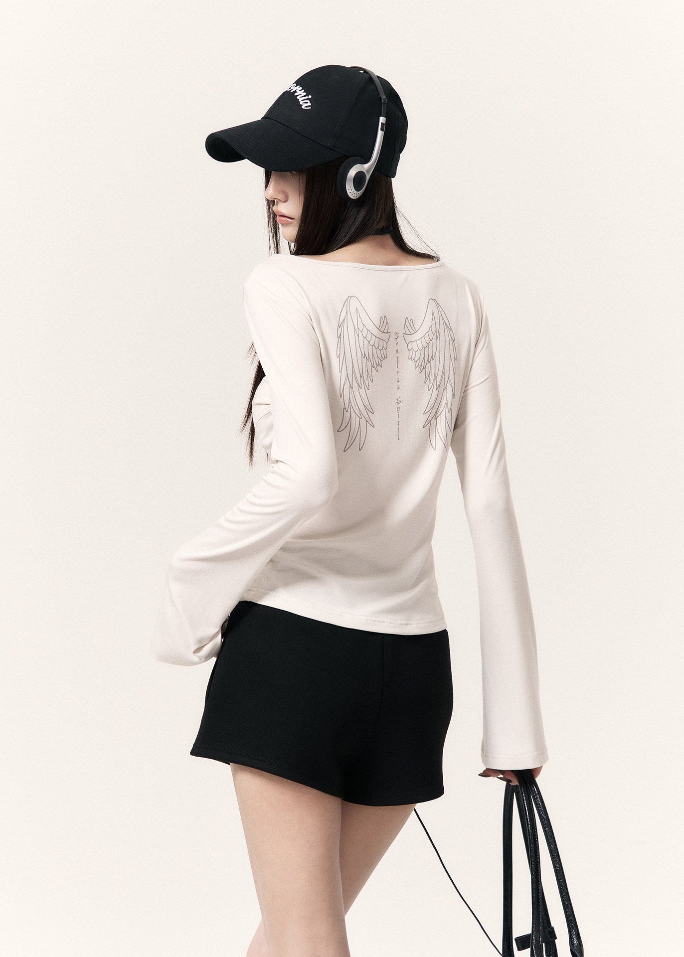 White long-sleeve top with an angel wing back print styled with a black mini skirt and cap