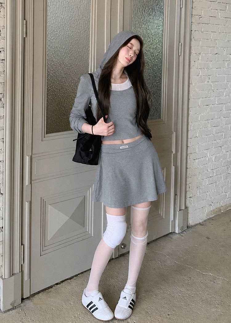 Model wearing a gray faux-layered hooded top and pleated mini skirt set