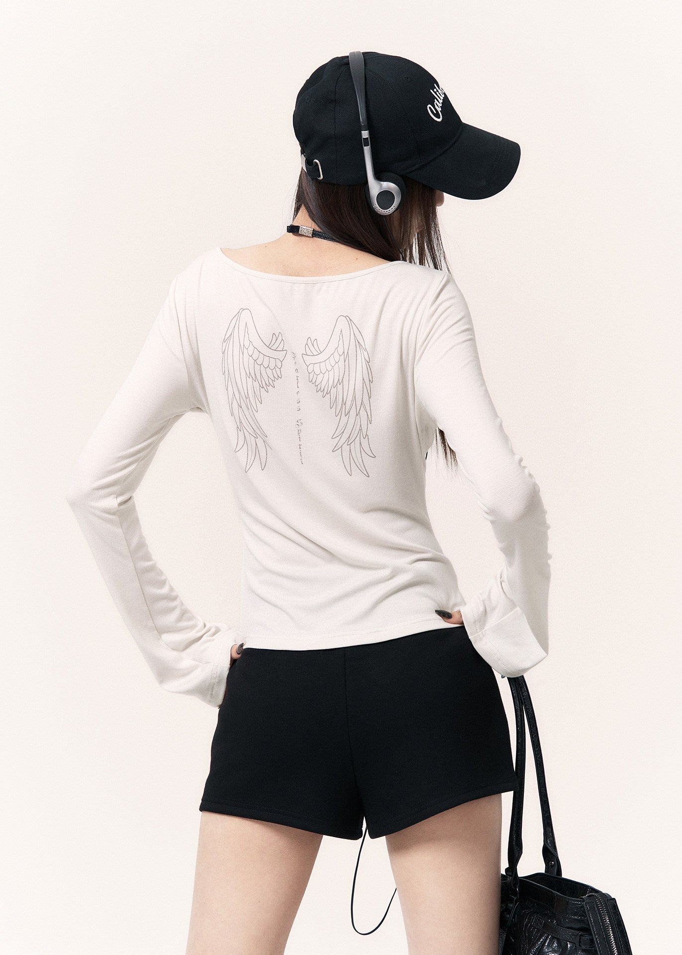 White long-sleeve top with an angel wing back print styled with a black mini skirt and cap