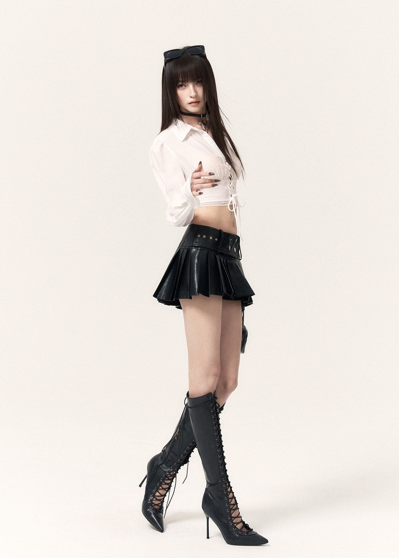 Model wearing a black pleated leather-look mini skort with a white cropped top