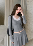 Model wearing a gray faux-layered hooded top and pleated mini skirt set