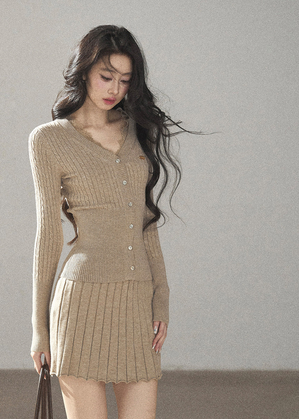 Women's ribbed knit cardigan styled with matching beige pleated mini skirt