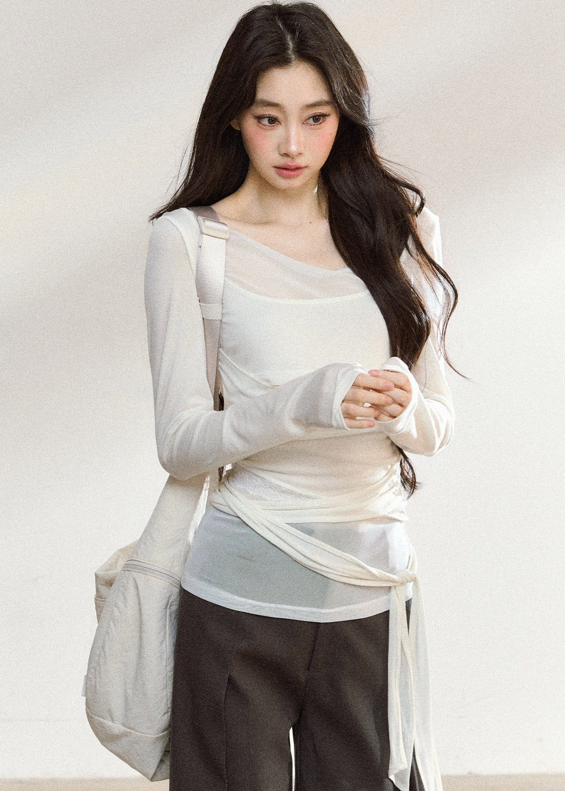 White asymmetric layered long-sleeve top with sheer panels and draped waist ties